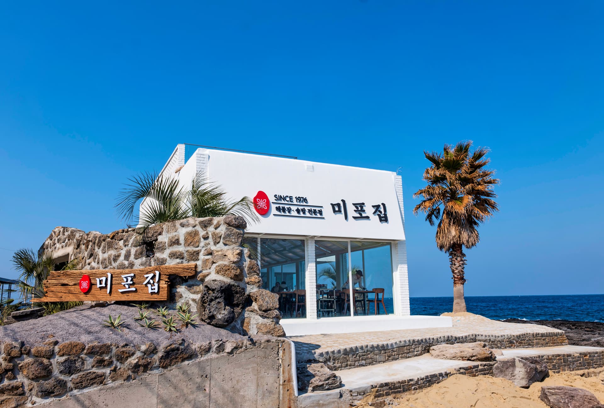 현무암 담장 위 미포집 간판과 바다를 마주한 매장 외관
